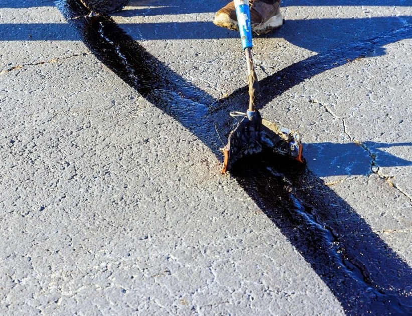 Hot rubberized crack sealant being squeegeed across an asphalt seam